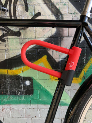 A CYCL Red Lock, a U-Lock with a hardened steel casing, securing a bicycle against a brick wall.