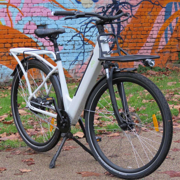 A white CYCL Carr-e e-bike parked in front of a colorful wall.