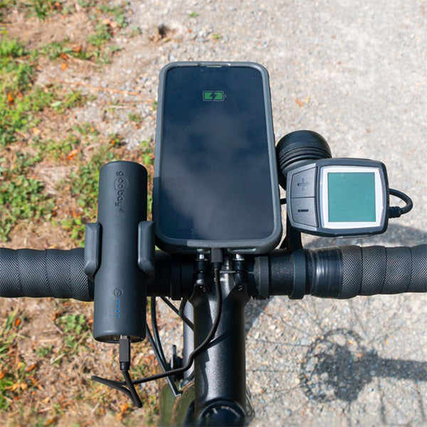 The handlebars of a bicycle now feature a handlebar mount with a CYCL Bike Power Bank, a mounted smartphone showing a charging symbol, and a bike computer/display. Equipped with Quick Charge technology, it ensures your devices stay powered throughout your ride.