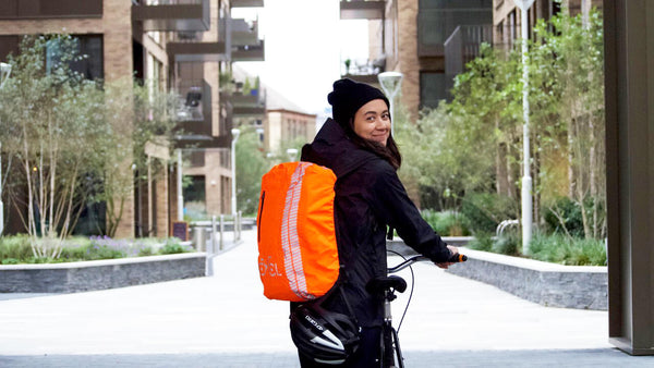 Woman on bicycle with high visibility backpack cover | CYCL